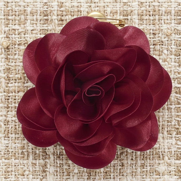 A large fabric artificial flower with layered ruffled petals in a deep burgundy red color, isolated on a white background.