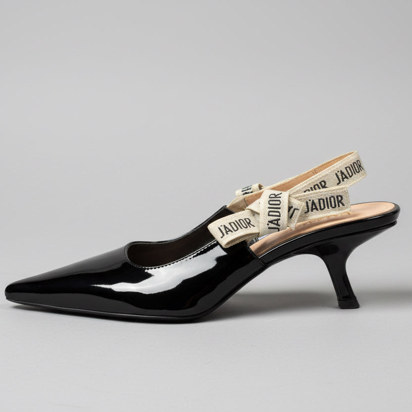 Black high-heeled shoe with 'JADior branding on a wooden surface.