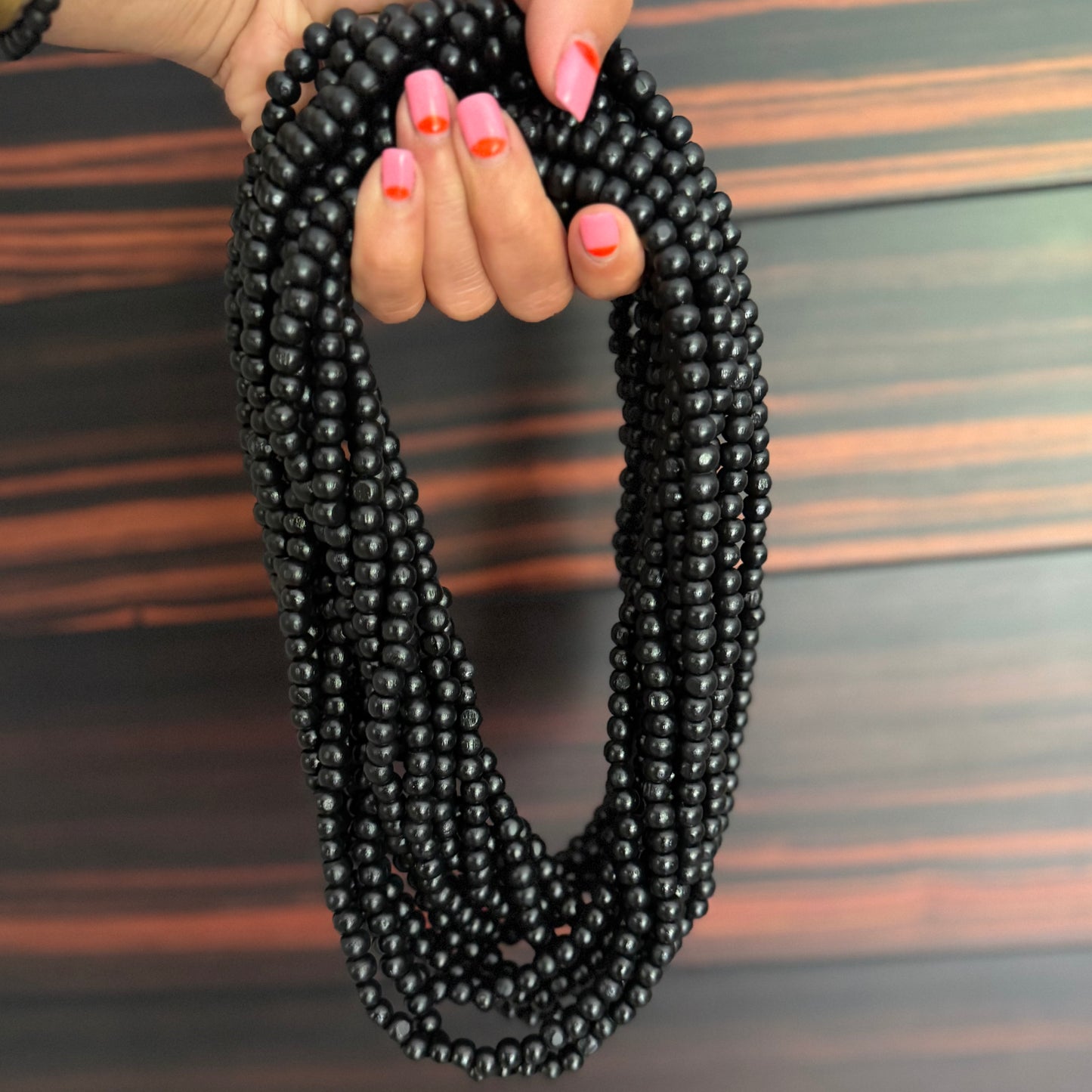 Black beaded necklace held by a hand with pink nail polish on a wooden surface