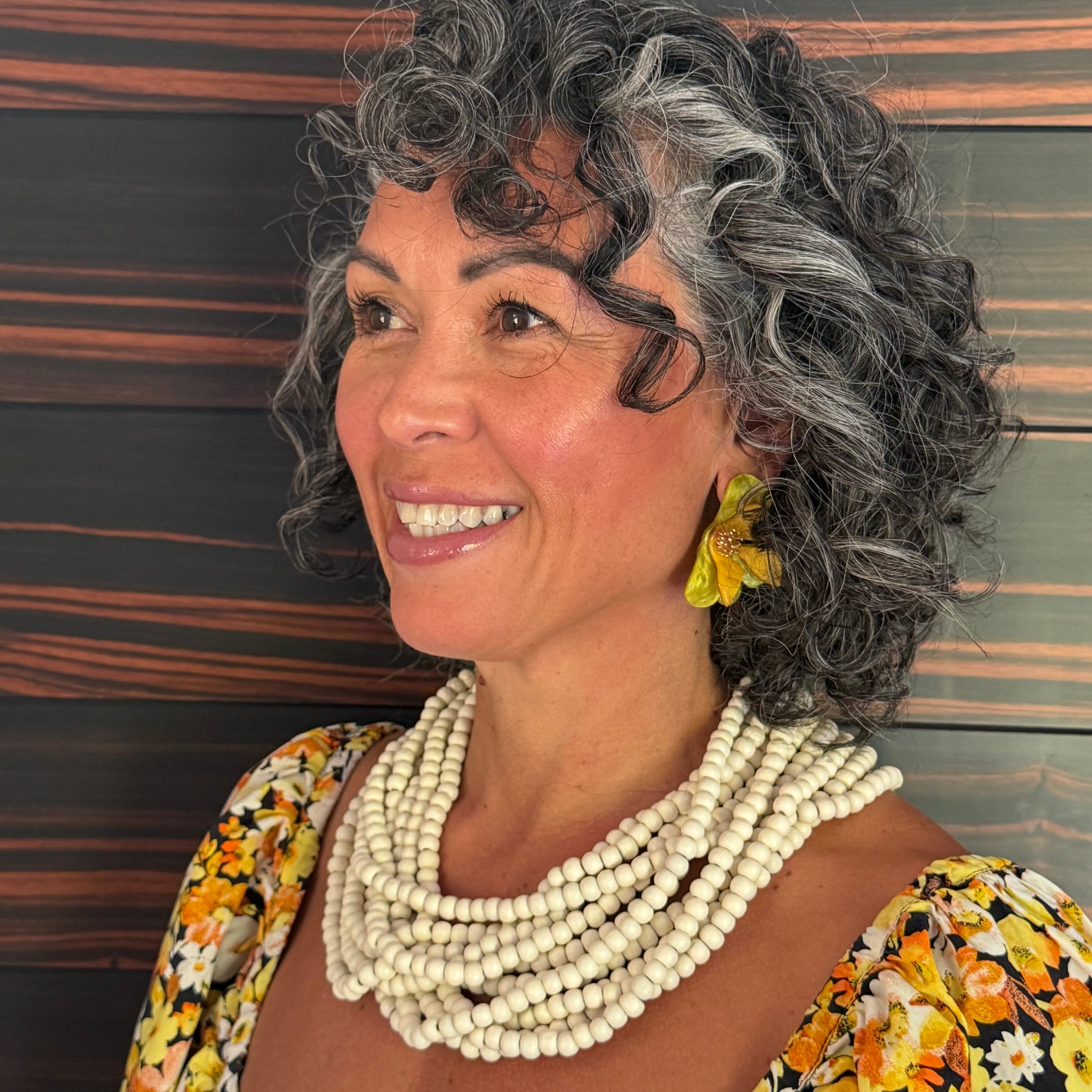 Woman with gray hair and beaded necklace against a striped background