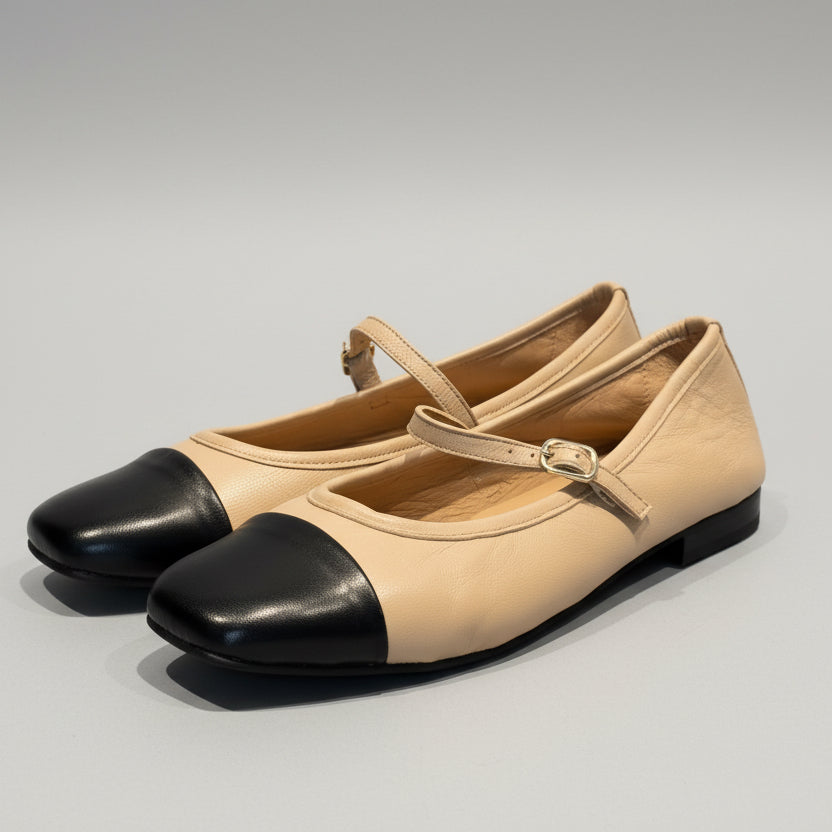 Pair of beige shoes with black toes on a wooden surface