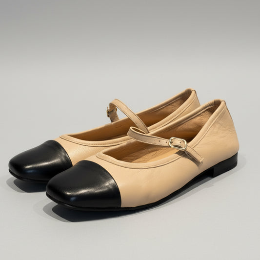 Pair of beige shoes with black toes on a wooden surface