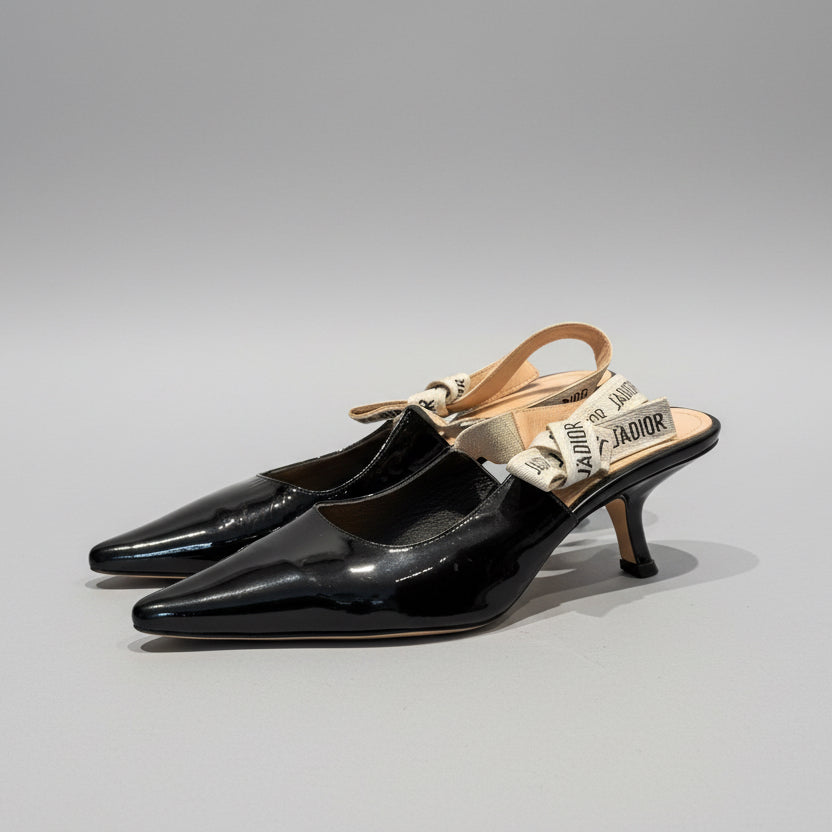 Black high-heeled shoes with a tan strap on a gray background