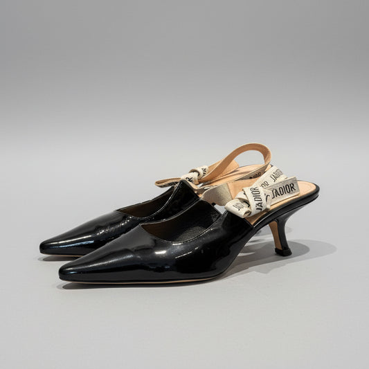Black high-heeled shoes with a tan strap on a gray background