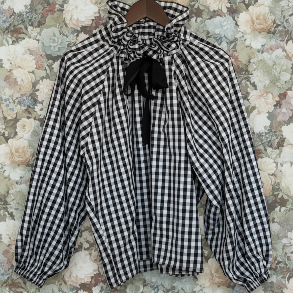 Black and white checkered blouse with a bow tie on a hanger against a white background