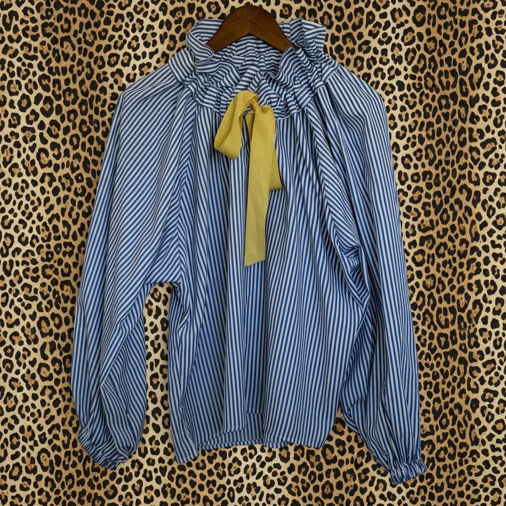 Blue and white striped blouse with a yellow ribbon on a wooden hanger against a leopard  background
