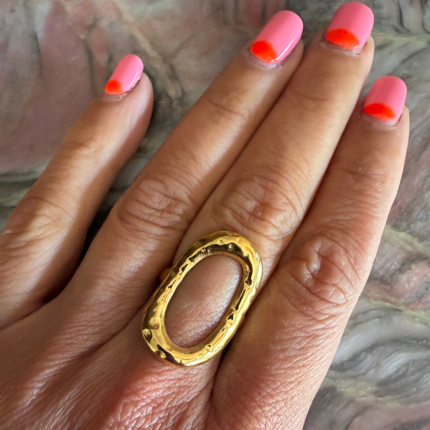 Gold ring on a hand with pink nail polish against a marble background
