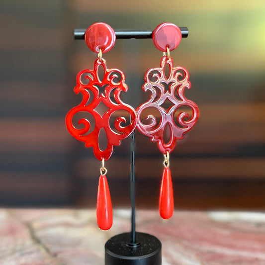 Red earrings with intricate designs on a black stand against a blurred background