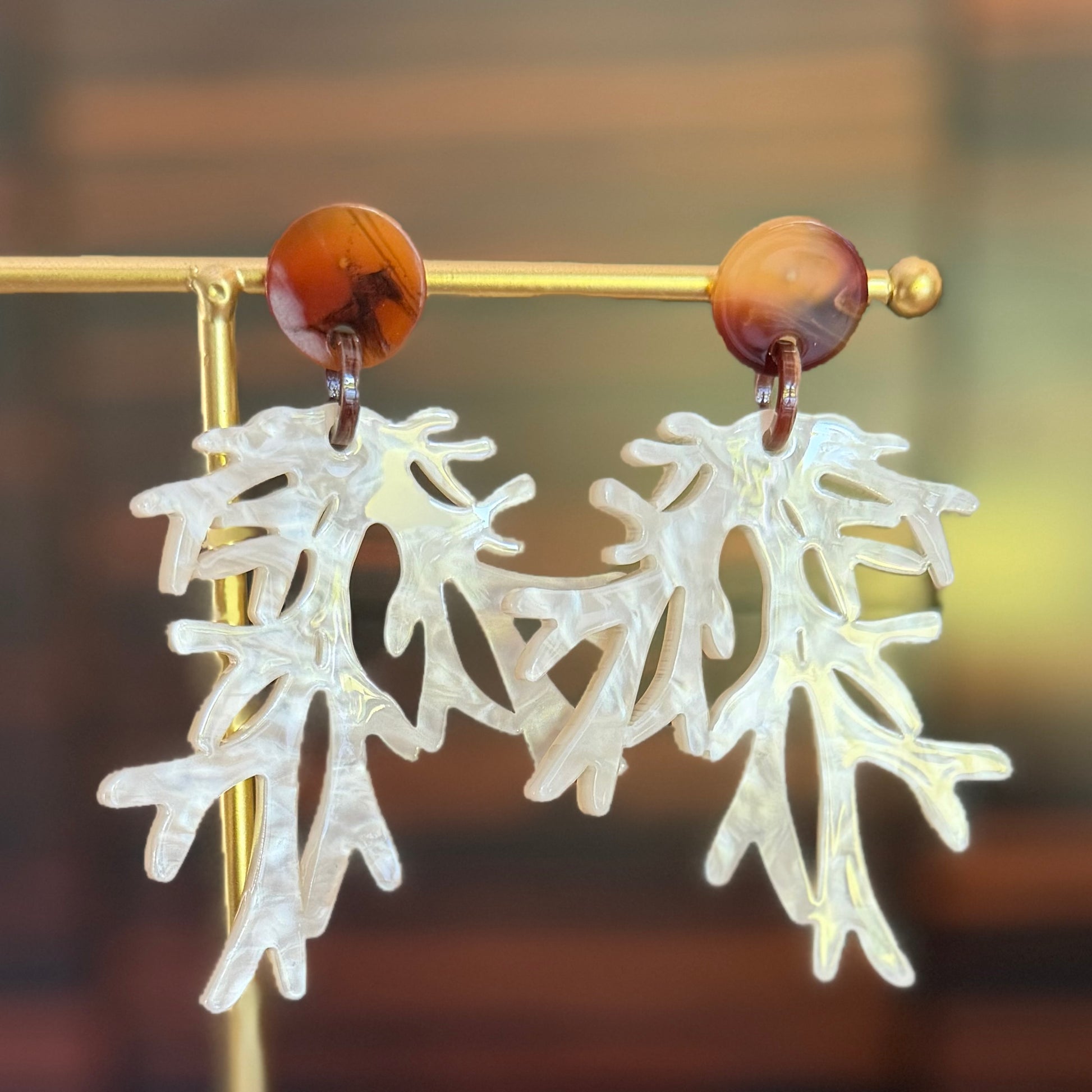 Pair of earrings with white leaf-like designs and wooden accents on a blurred background