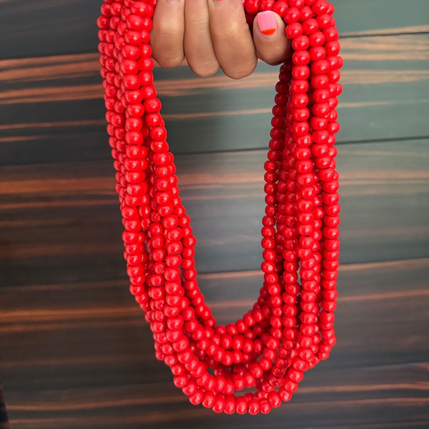 Red beaded necklace held by a hand against a wooden background