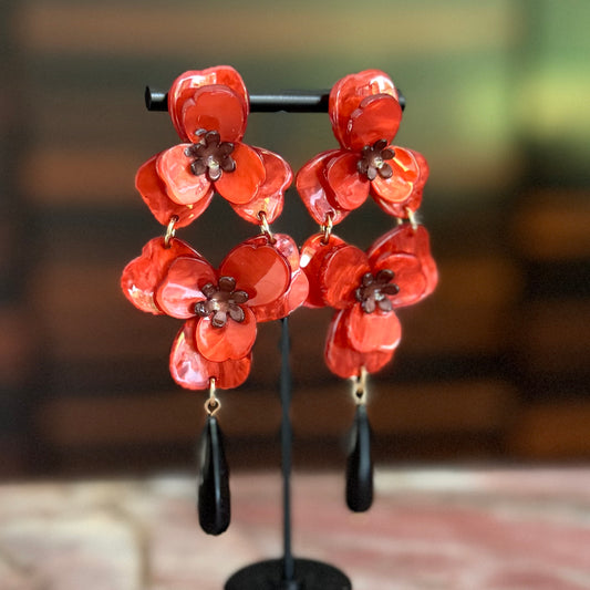 Floral earrings with red flowers and black accents on a stand against a blurred background