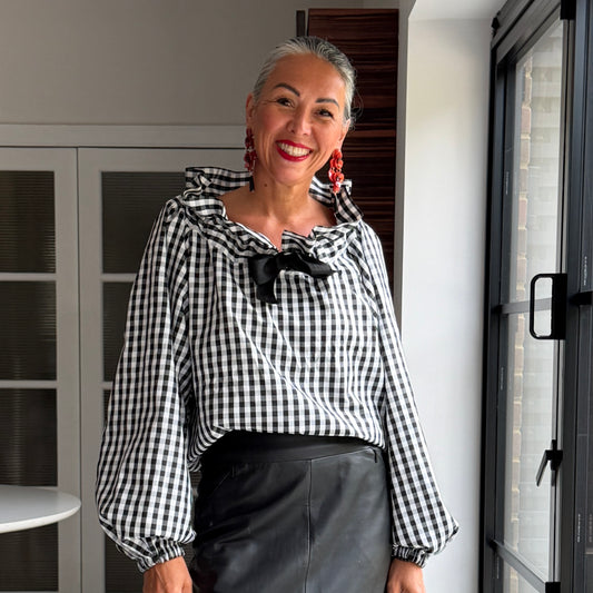 Woman wearing a black and white checkered blouse with a large bow standing indoors.