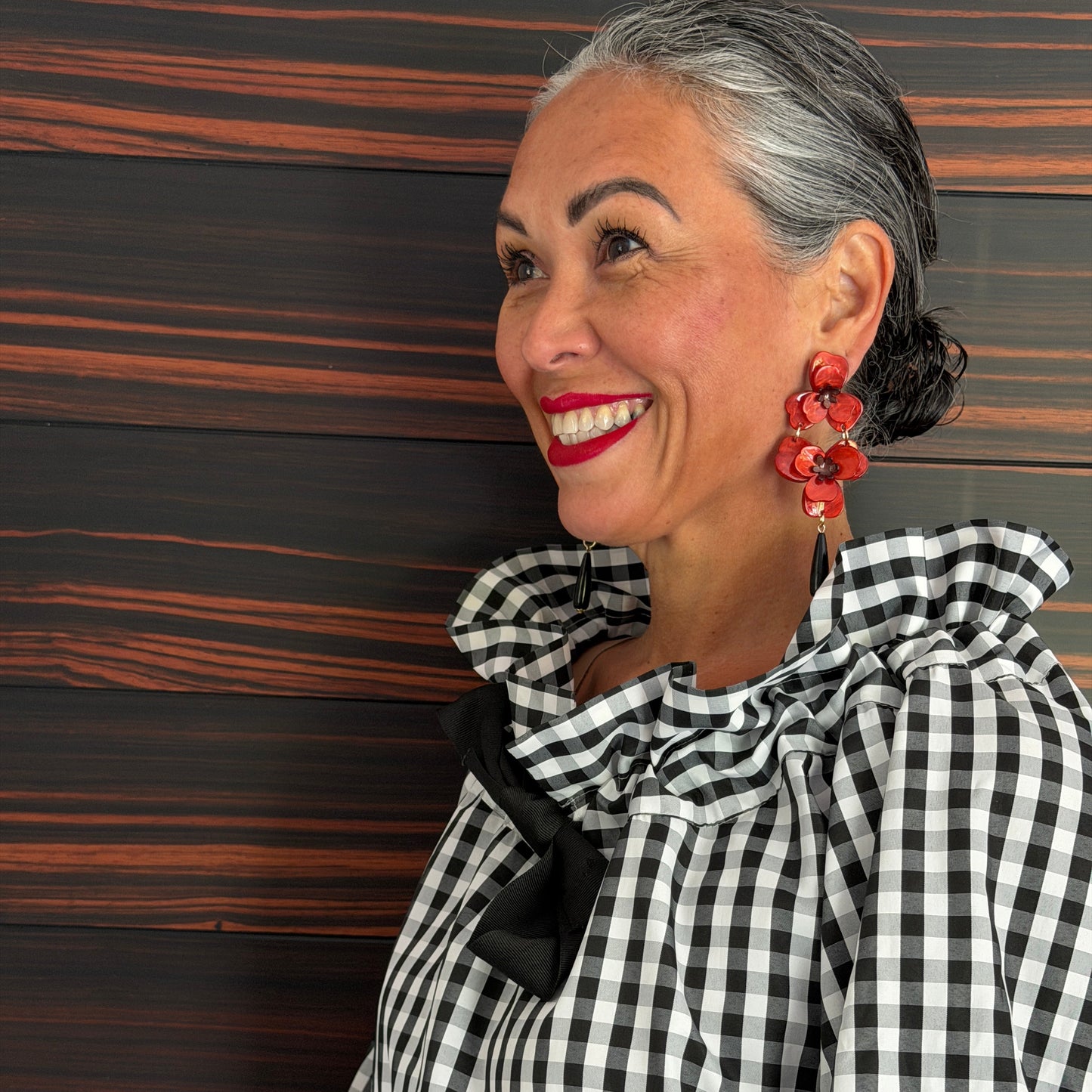 Woman wearing a black and white checkered outfit with red earrings against a wooden background