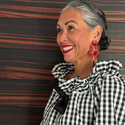 Woman wearing a black and white checkered outfit with red earrings against a wooden background