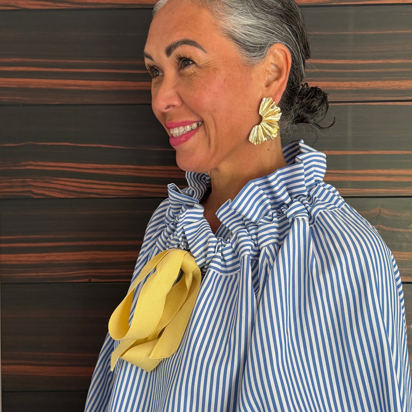 Person wearing a blue and white striped shirt with yellow gloves against a striped background