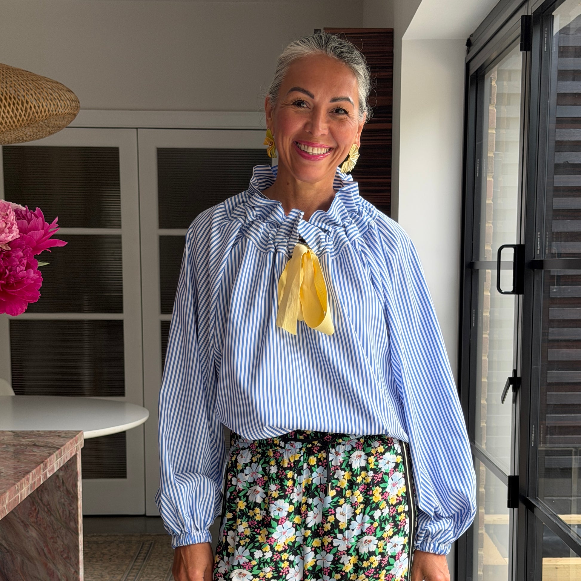 Woman wearing a blue striped shirt with a yellow bow and floral skirt in an indoor setting.