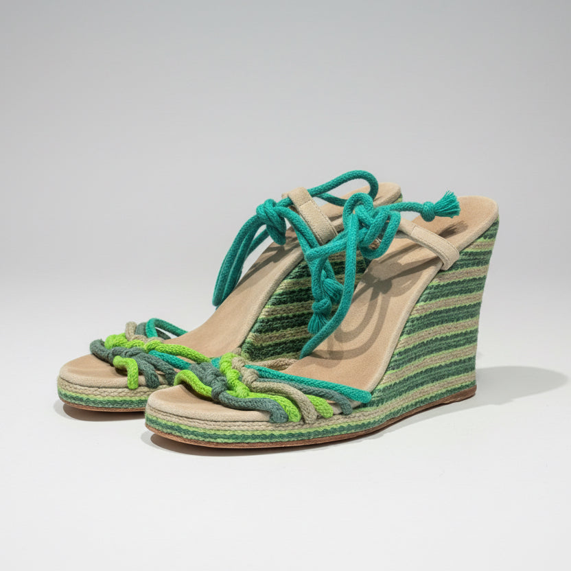 Woven wedge sandals with green and blue straps on a wooden surface.