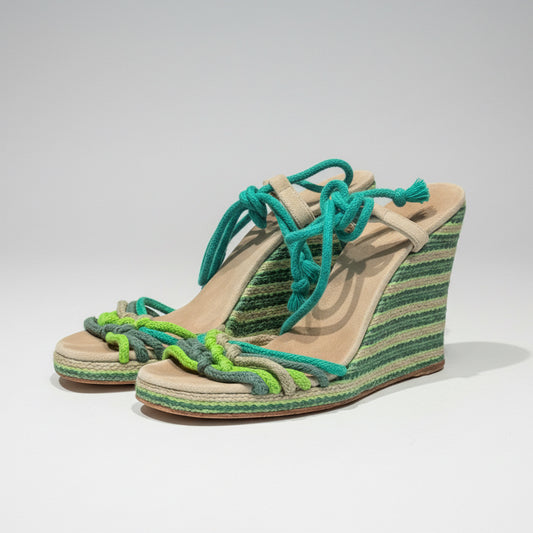 Woven wedge sandals with green and blue straps on a wooden surface.