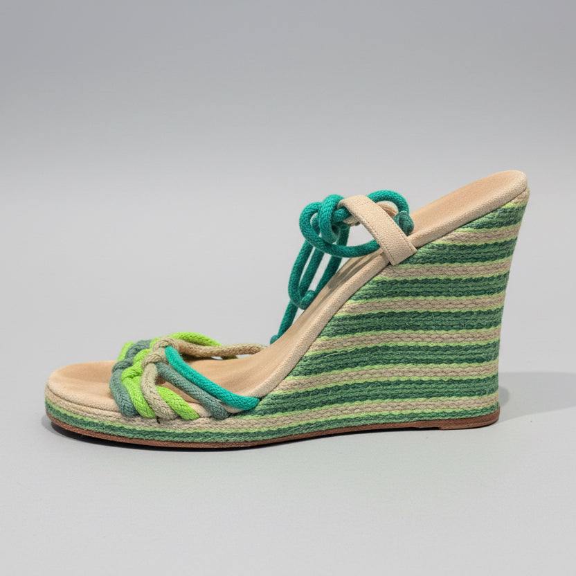 Green wedge sandal with braided design on a wooden surface