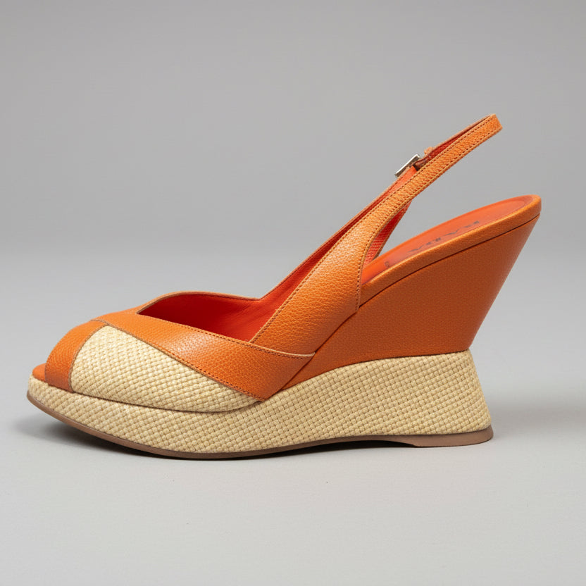 Orange wedge sandal on a wooden surface with a neutral background