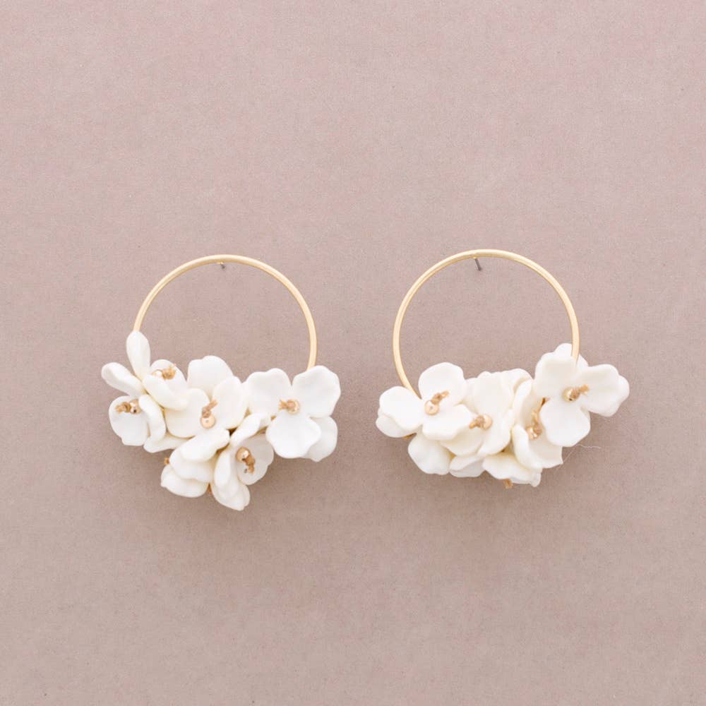 Pair of gold hoop earrings with white floral attachments on a beige background