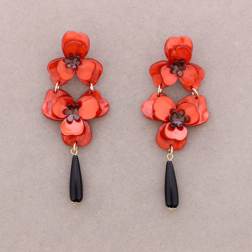Red floral earrings with black teardrop pendants on a beige background