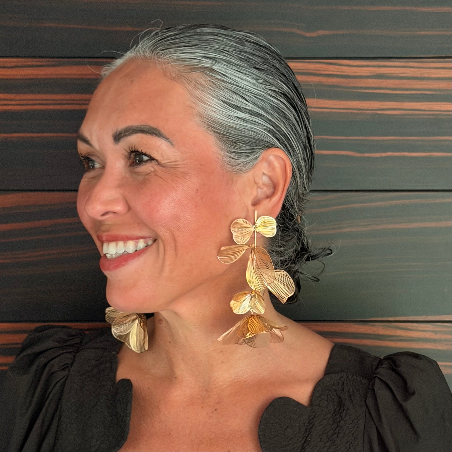 Woman wearing gold leaf earrings against a wooden background