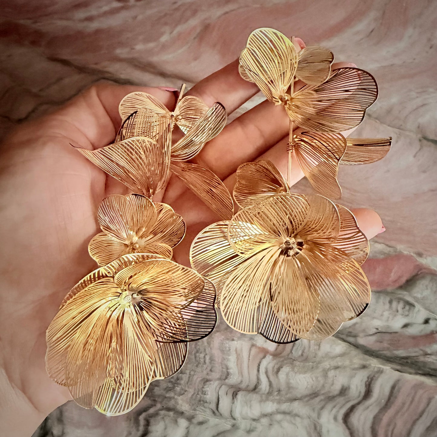 Gold floral earrings held in a hand against a marble background
