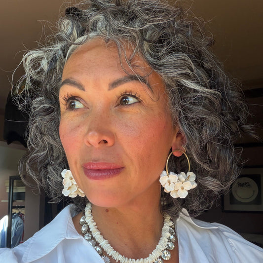 Woman with gray hair wearing large hoop earrings and a white top indoors.