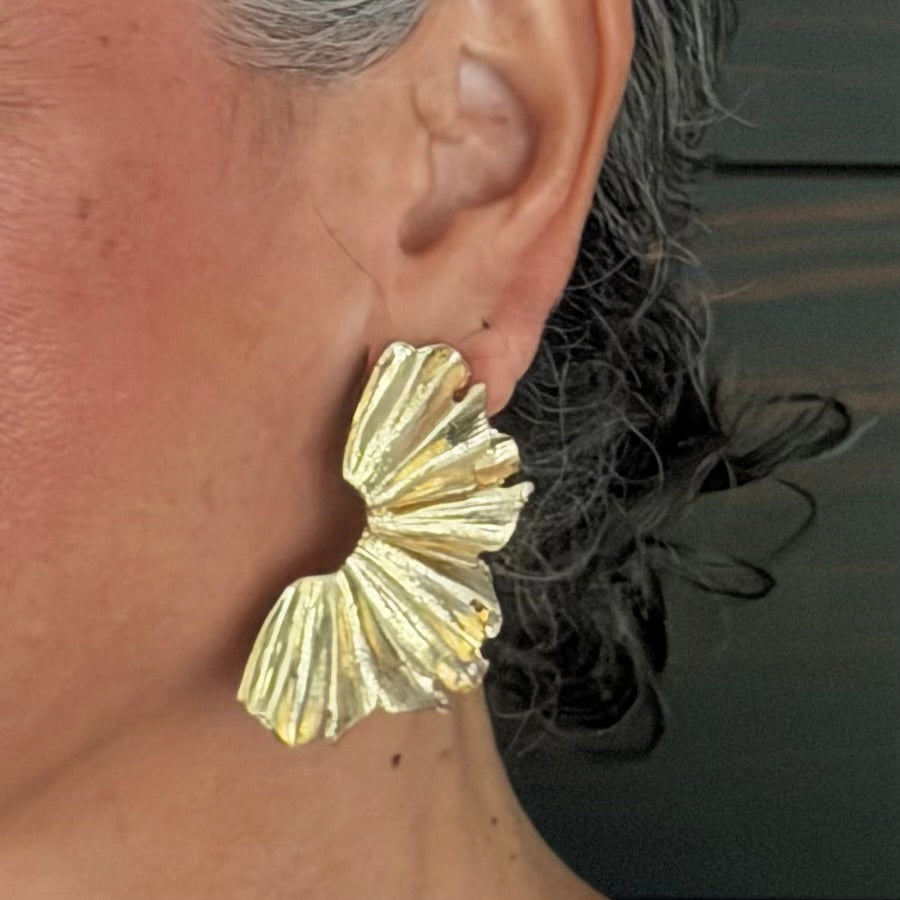 Gold leaf-shaped earring worn by a person with dark hair.