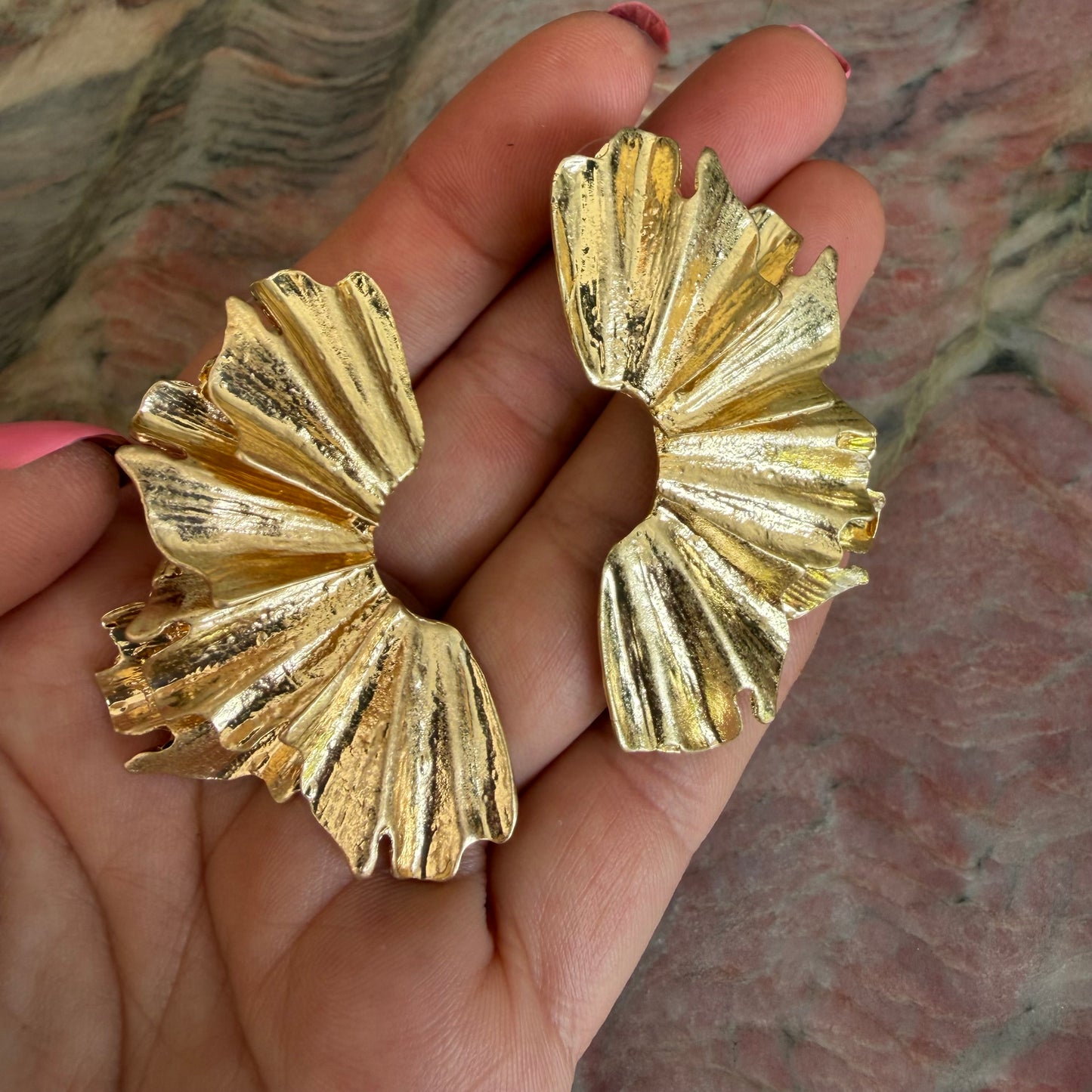 Gold butterfly-shaped earrings held in a hand against a marble background