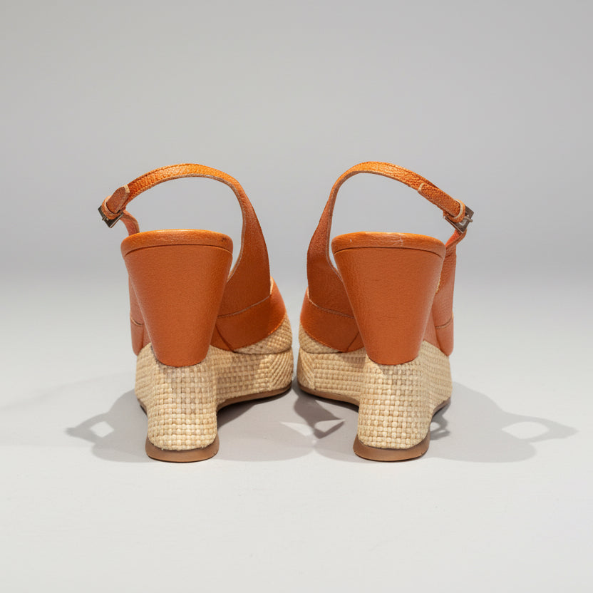 Pair of orange wedge  sandals with woven soles on a wooden surface