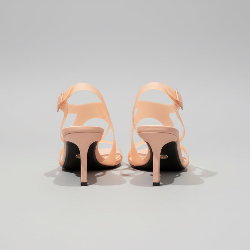Pair of beige high-heeled sandals on a wooden surface with a light gray background